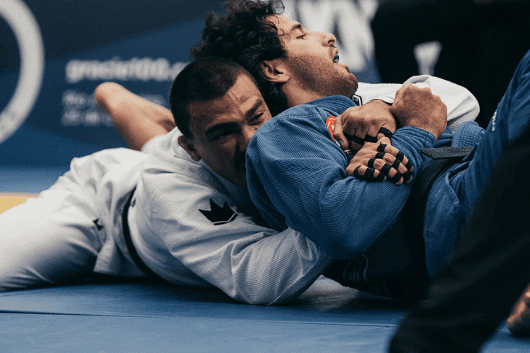 Two jiu-jitsu fighters grappling on the mat, one in a white gi holding the other in a blue gi.